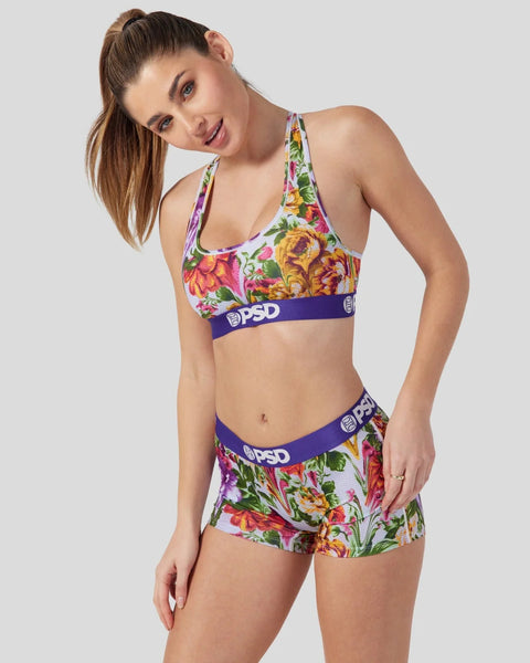 Woman wearing a colorful floral sports bra and matching shorts set with purple PSD waistband details.