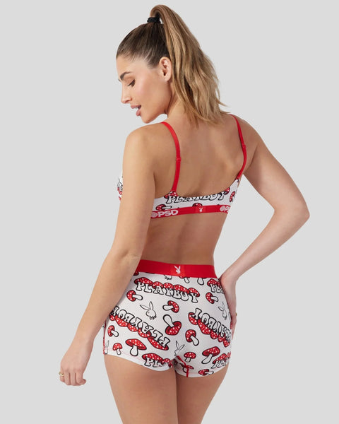 Woman wearing red and white Playboy-branded bralette and shorts with mushroom print design.