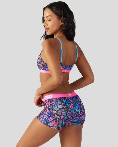 Woman wearing a three-piece lingerie set with blue straps, pink and purple butterfly print, and pink waistband trim.