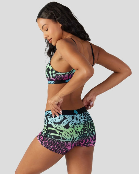 Woman wearing colorful sports bra and shorts set with checkered, neon, and abstract graphic patterns in green, pink, and blue