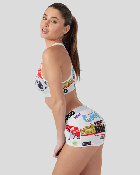 Woman wearing white sports bra and shorts with colorful food package graphics and text print.