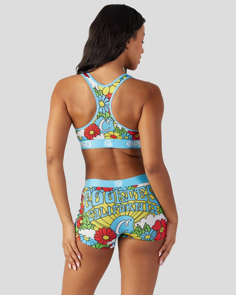 Woman wearing a colorful floral and text print sports bra and matching shorts set with blue, red, and yellow flowers.