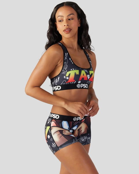 Woman wearing black Looney Tunes Taz sports bra and shorts set with colorful graphic print and PSD branding.