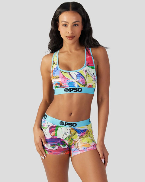 Woman wearing colorful Looney Tunes print sports bra and shorts with blue waistbands and PSD branding.