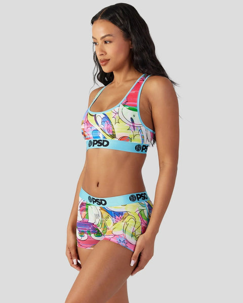 Woman wearing colorful Looney Tunes print sports bra and shorts with blue elastic waistband.