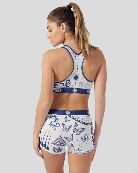Woman wearing white and navy sports bra and shorts with tattoo-inspired butterfly and geometric print design.