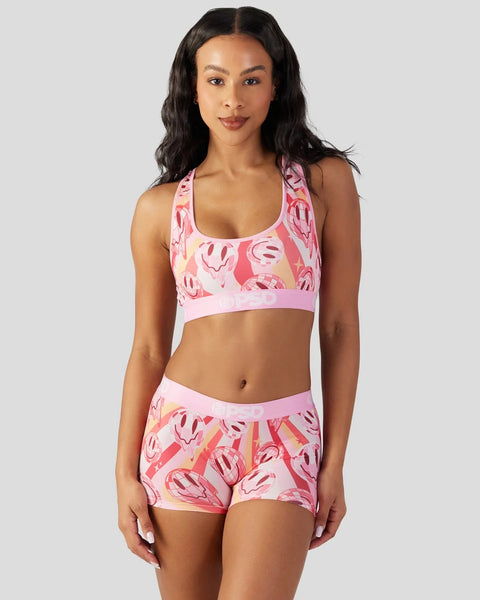 Women's sports bra and shorts set with pink smiley face print and white trim.