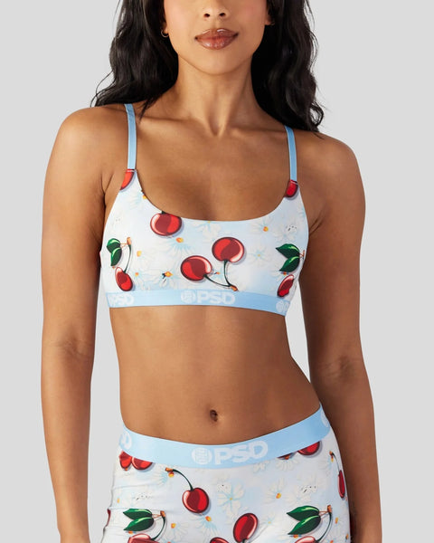 White sports bra with red cherry and daisy print, blue straps and waistband.