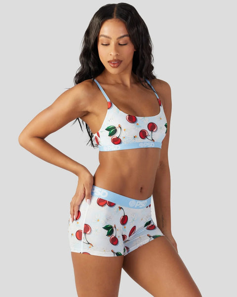 Woman wearing a two-piece set with light blue and white fabric featuring red cherry print and blue trim details.