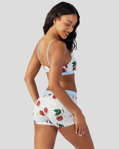 Two-piece swimsuit with cherry print on light blue and white background, featuring thin shoulder straps and matching shorts.