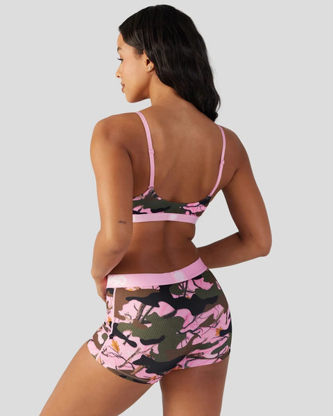 Woman wearing pink and black camouflage sports bra and matching shorts with side lacing detail, shown from back.