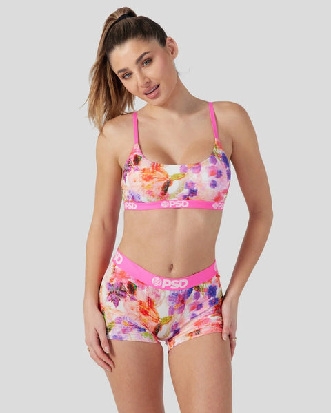 Woman wearing a two-piece lingerie set with pink straps and multicolored floral pattern on white background.