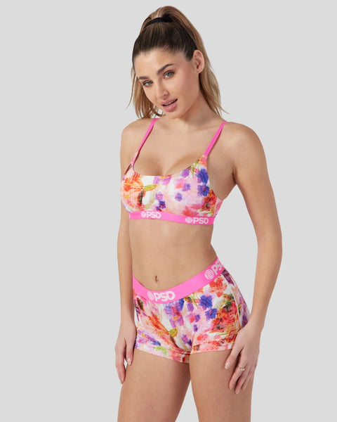 Woman wearing pink sports bra and matching shorts with multicolored floral print and branded waistband.