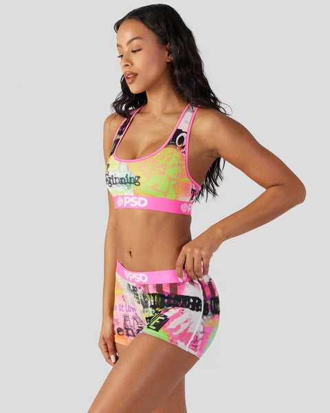 Woman wearing neon green and pink sports bra with matching shorts featuring colorful graphic prints and branded elastic bands