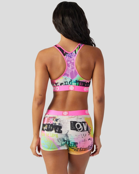 Women's sports bra and shorts set with colorful abstract print, pink trim, and text graphics on back view.