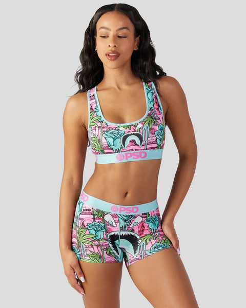 Woman wearing colorful graphic sports bra and matching shorts with pink, turquoise, and lime green floral print design.