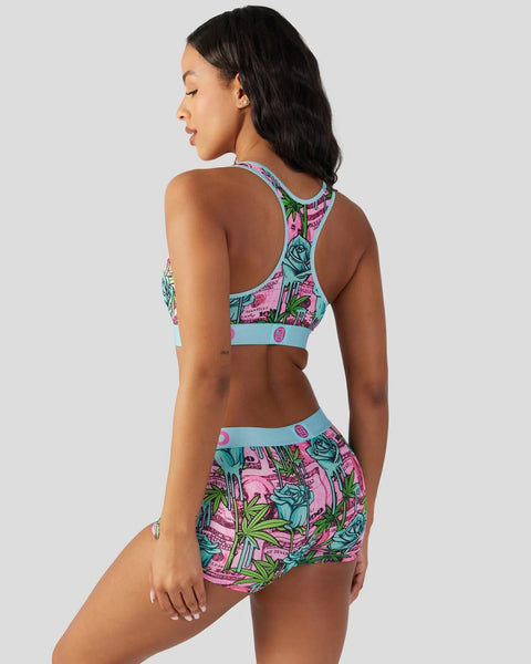 Woman wearing a colorful floral print sports bra and shorts set in pink, turquoise, and green, shown from the back.
