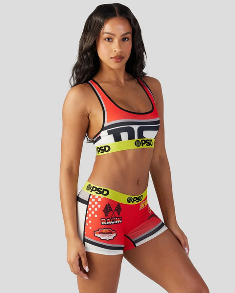 Woman wearing red, black, and white sports bra with neon yellow PSD waistband and matching red racing-themed shorts with grap