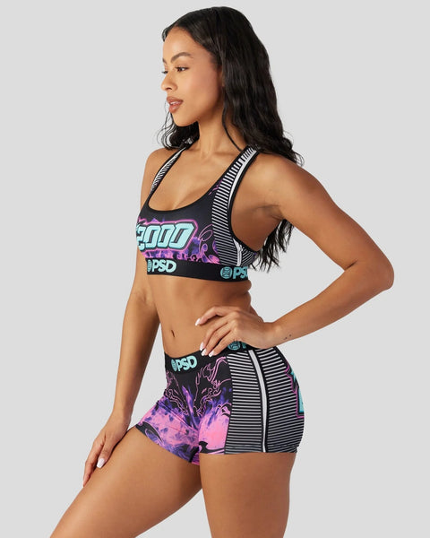 Woman wearing black sports bra and matching shorts with neon blue and pink graphic print and striped trim details.