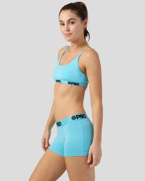 Woman wearing a turquoise sports bra and matching shorts with black waistband branding.