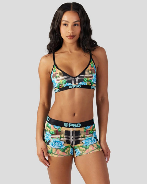 Woman wearing tartan and floral patterned sports bra and matching shorts with black trim and branded waistband.