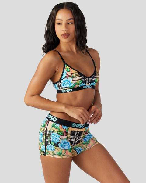 Woman wearing black sports bra and shorts with blue roses and tartan pattern, black straps and PSD waistband.