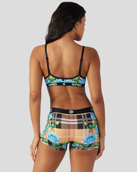 Woman wearing black-strap sports bra and matching shorts with tartan plaid and blue floral pattern design.