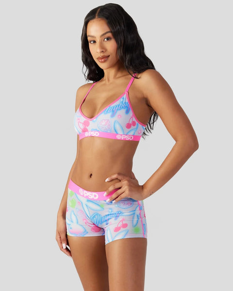 Woman wearing pink and blue patterned sports bra and matching shorts with branded elastic bands.