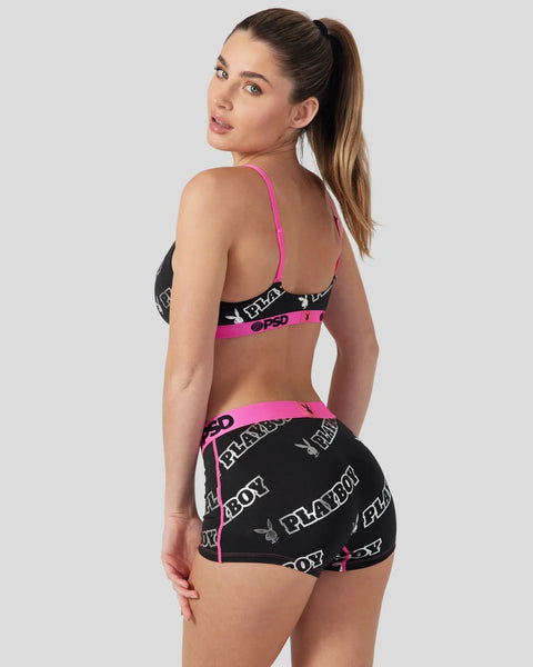 Woman wearing black Playboy-branded bra and shorts with pink trim and logo detailing.