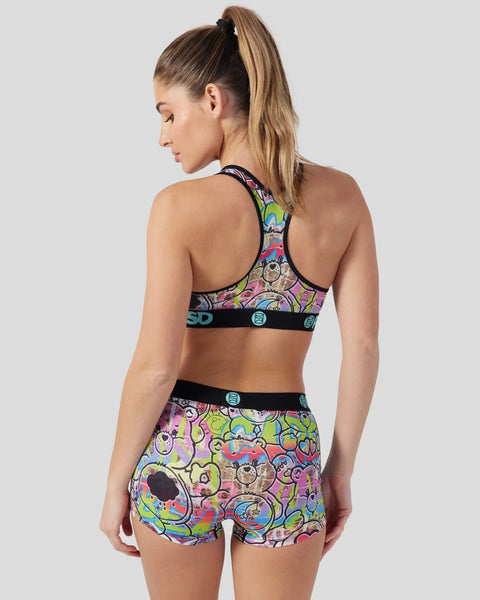 Woman wearing colorful Care Bears-patterned sports bra and shorts with black trim and branding details.