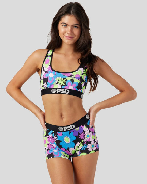 Woman wearing colorful floral print sports bra and matching shorts with black PSD waistbands on white background.