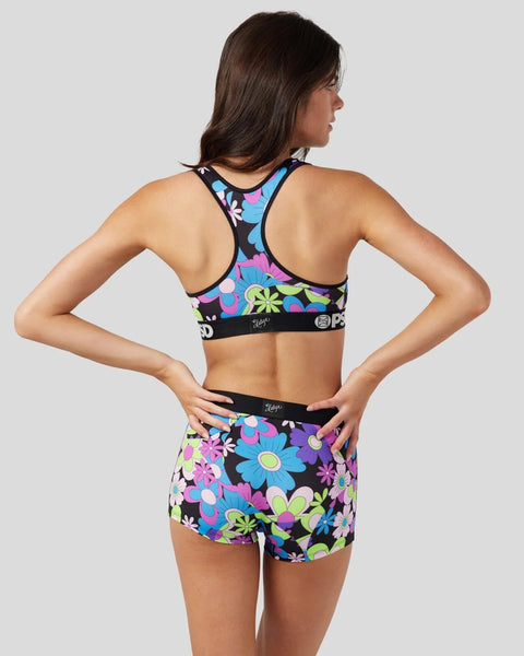 Woman wearing a black sports bra and shorts with colorful floral pattern in pink, blue, yellow, and purple.