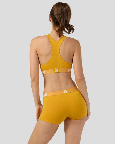 Woman wearing mango-yellow racerback sports bra and matching shorts with branded waistband, viewed from back.