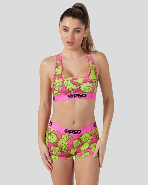 Woman wearing neon pink and lime green sports bra and shorts set with cartoon character print and PSD branding.