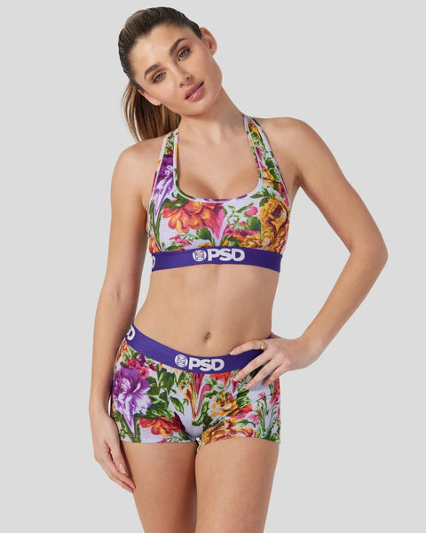 Woman wearing colorful floral print sports bra and matching shorts with purple PSD waistband.
