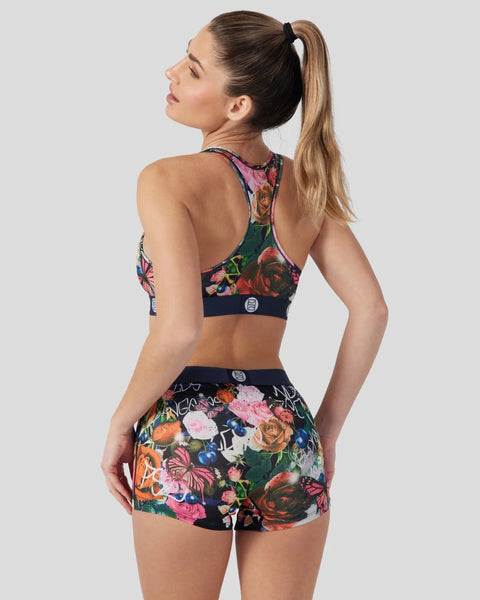 Woman wearing a floral patterned sports bra and shorts set in navy with pink, orange, and green flowers.