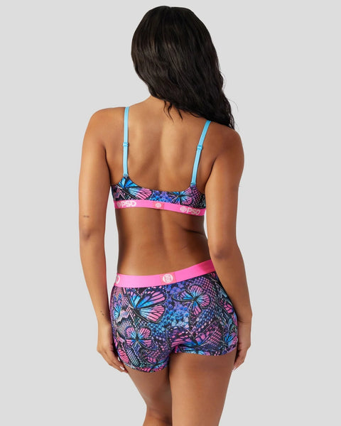 Woman wearing two-piece swimsuit with blue straps, pink waistband, and colorful butterfly and geometric print on dark backgro