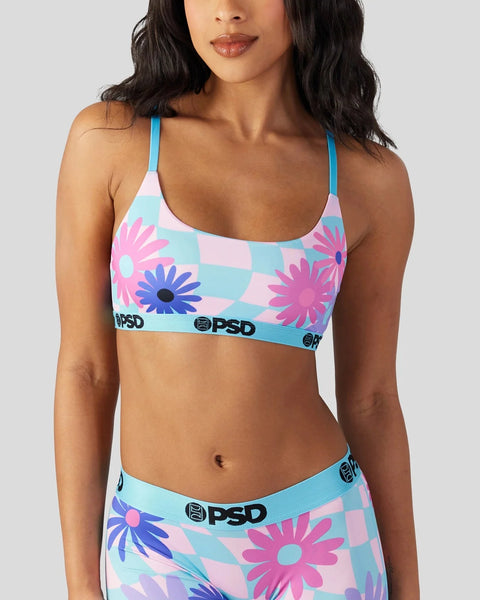 Woman wearing blue strapped sports bra with pink, purple, and blue checkered floral pattern and PSD branding.