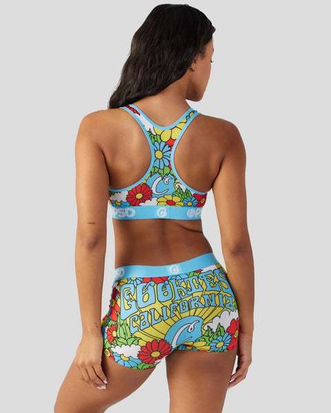 Woman wearing blue sports bra and shorts with colorful floral and text print design, shown from back view.
