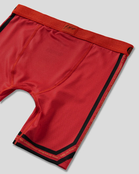 Red boxer briefs with black waistband and side stripe trim, featuring small logo on waistband.
