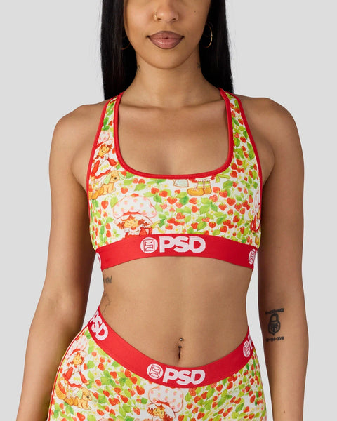Woman wearing a red and cream sports bra with strawberry and character print, red trim, and PSD branding.