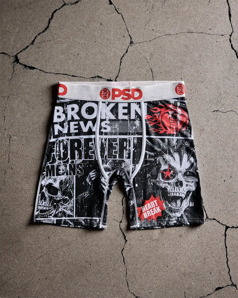 PSD black and white boxer briefs with "Broken News" text, skull graphics, and red accents on cracked concrete background.