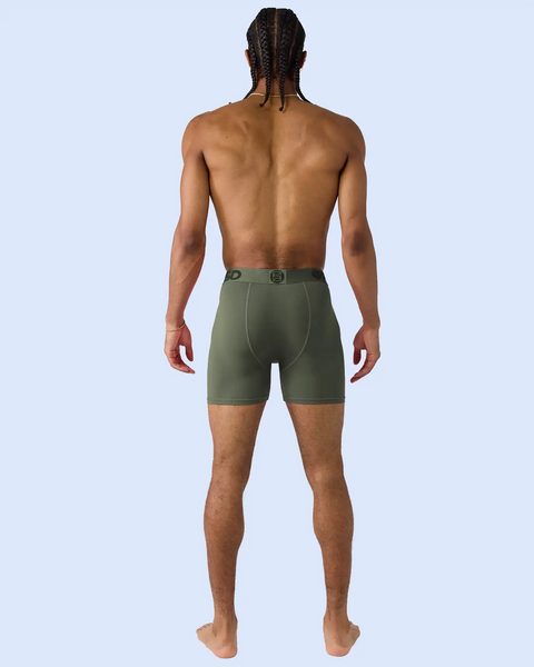 Man wearing forest green shorts with button waistband, shown from behind against light blue background.