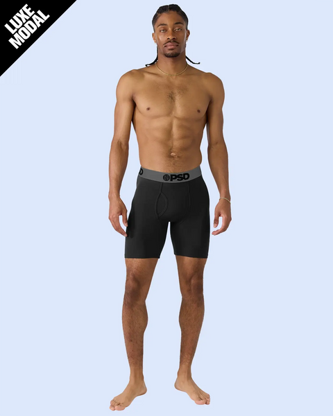 Man wearing black boxer briefs with grey waistband against light blue background.