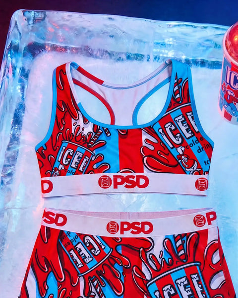 Red and blue ICEE-branded sports bra and shorts set with PSD waistbands, displayed on icy background.