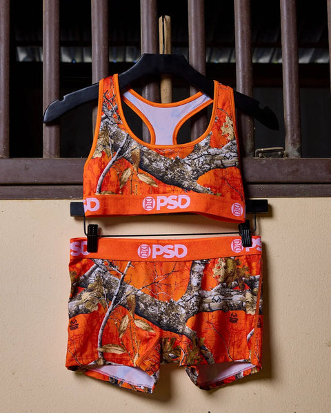 Orange Realtree camouflage sports bra and shorts set with PSD branding on hanger.