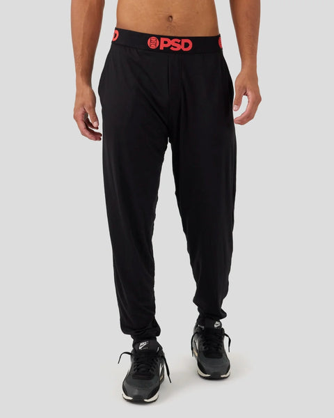 Black lounge pants with red PSD waistband, tapered ankles, worn with black sneakers.