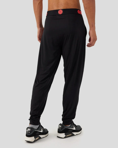 Black lounge pant with red button details at waist, tapered legs, worn with black and white sneakers.