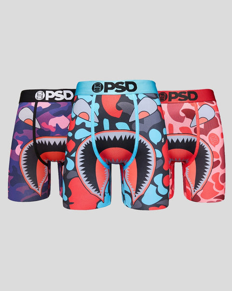 Three PSD boxer briefs with camouflage patterns and cartoon monster face designs in purple, blue, and red colorways.