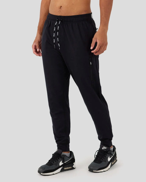 Black joggers with drawstring waist, side pockets, and tapered ankles worn with black and white sneakers.